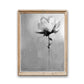A framed grayscale painting of a single flower. The flower is rendered in a loose, expressive style with shades of gray and white. The background is a textured gray canvas. The painting is in a light beige wooden frame.  The artist's signature is visible at the bottom. The overall style is modern and abstract.