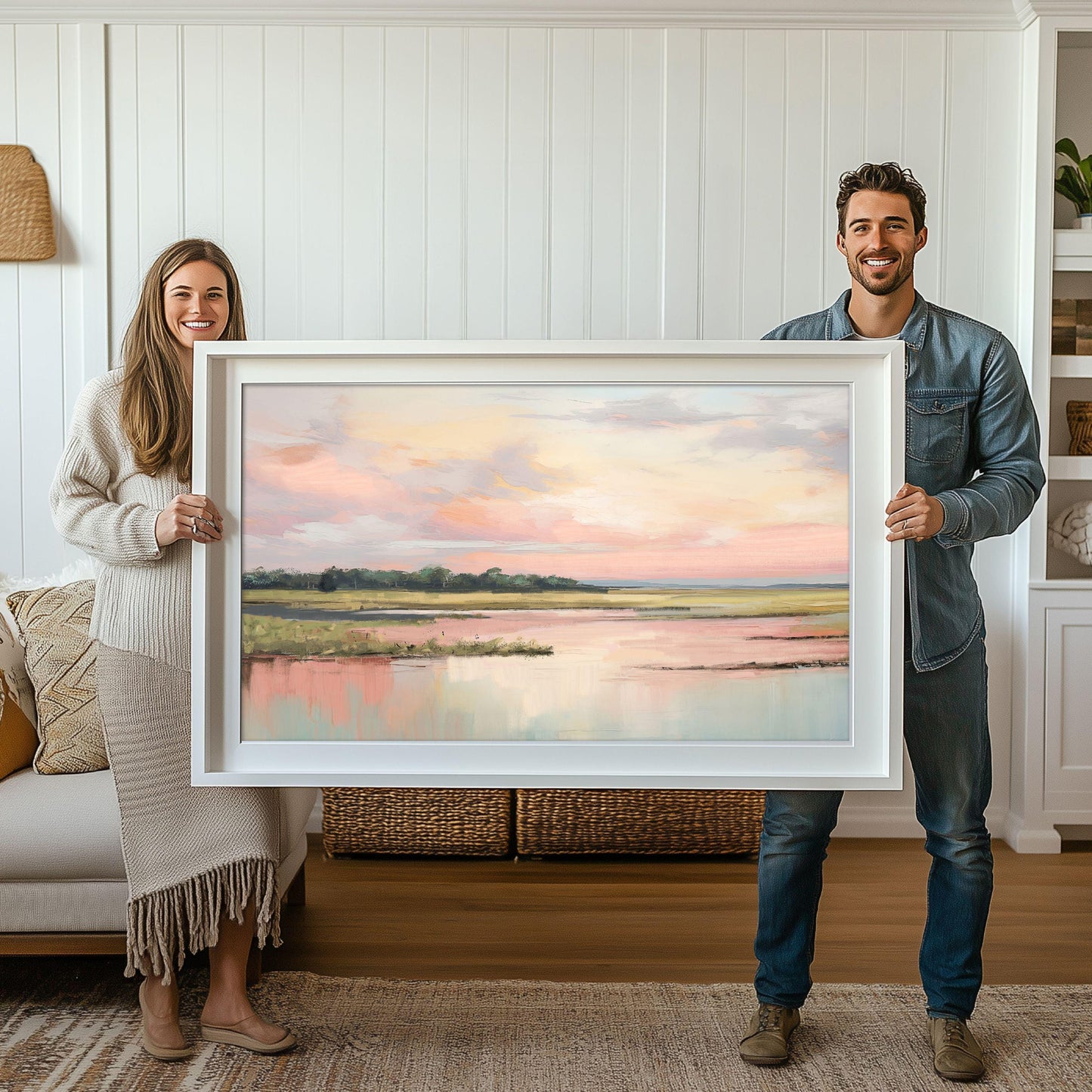 May include: A framed landscape painting of a lake with a pink and blue sky. The painting is in a white frame and is being held by two people.