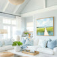 May include: A bright, airy living room with white sofas, light blue pillows, and a framed landscape painting. A woven light fixture hangs from the ceiling. The room has a coastal, relaxed vibe, with a white coffee table and decorative tray.