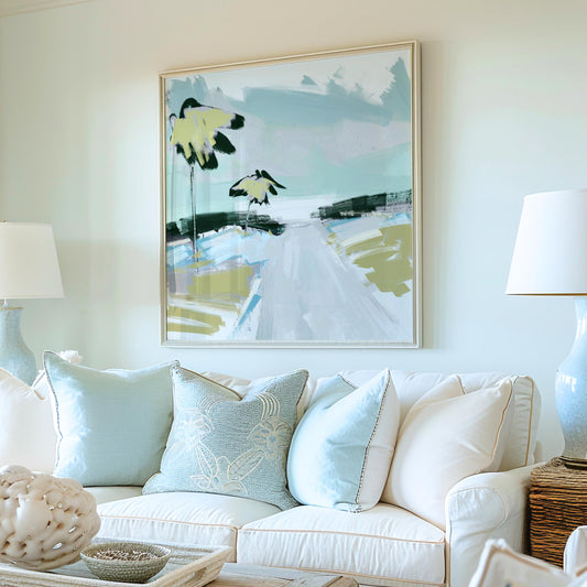 May include: An abstract painting in a silver frame hangs above a white sofa with light blue pillows. The artwork features yellow and black floral shapes and a road in shades of blue, green, and white. Two matching lamps flank the sofa.